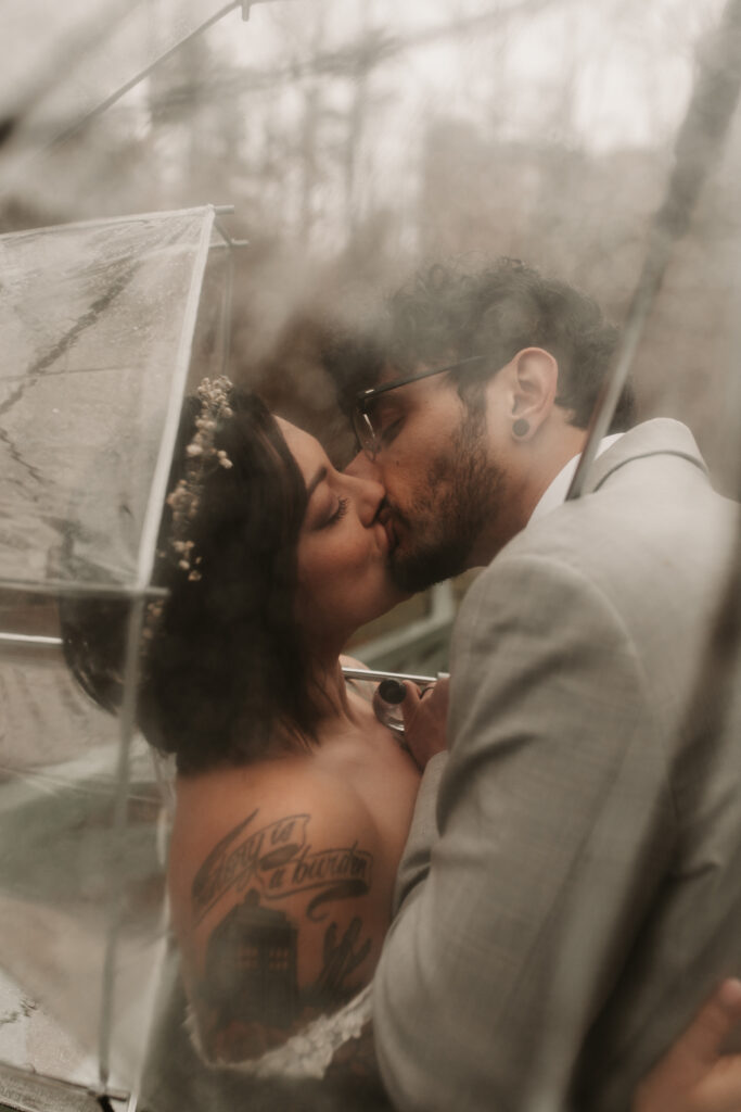 Artistic image of a couple kissing during their elopement through a clear umbrella in Asheville North Carolina