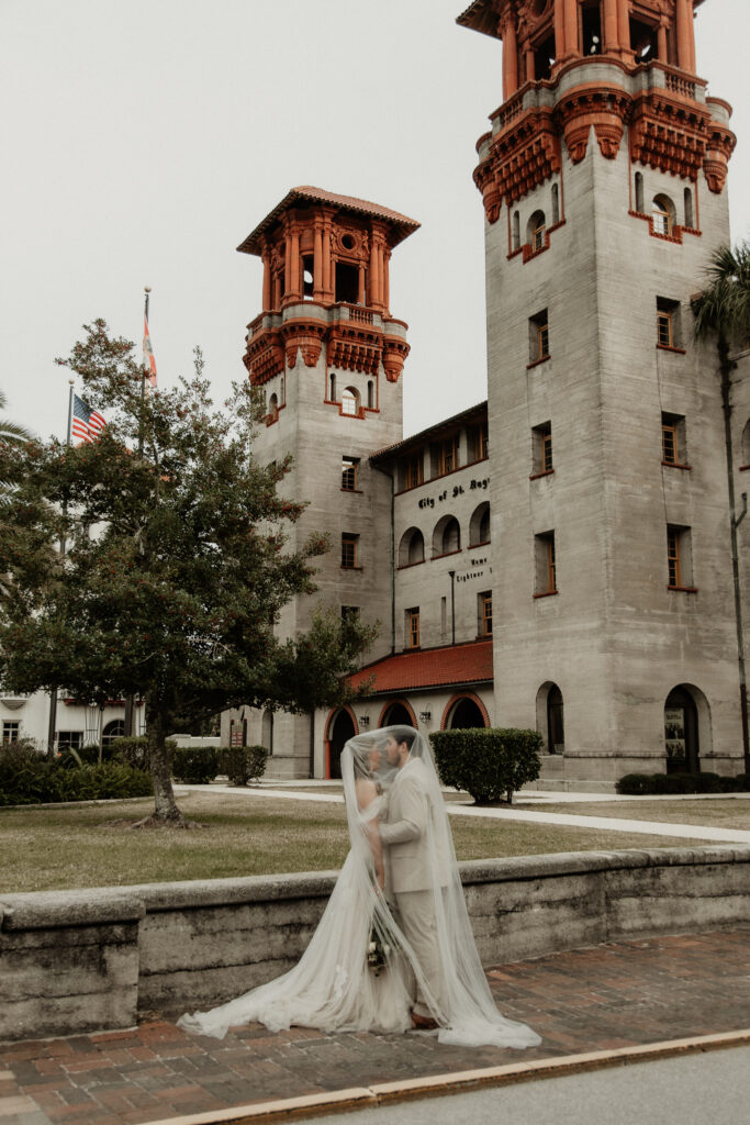 Bride and groom are under the brides veil kissing on the cobble stone side walk of st augustine