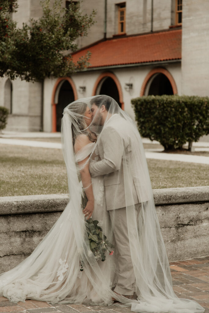 Bride and groom are under the brides veil kissing on the cobble stone side walk of st augustine