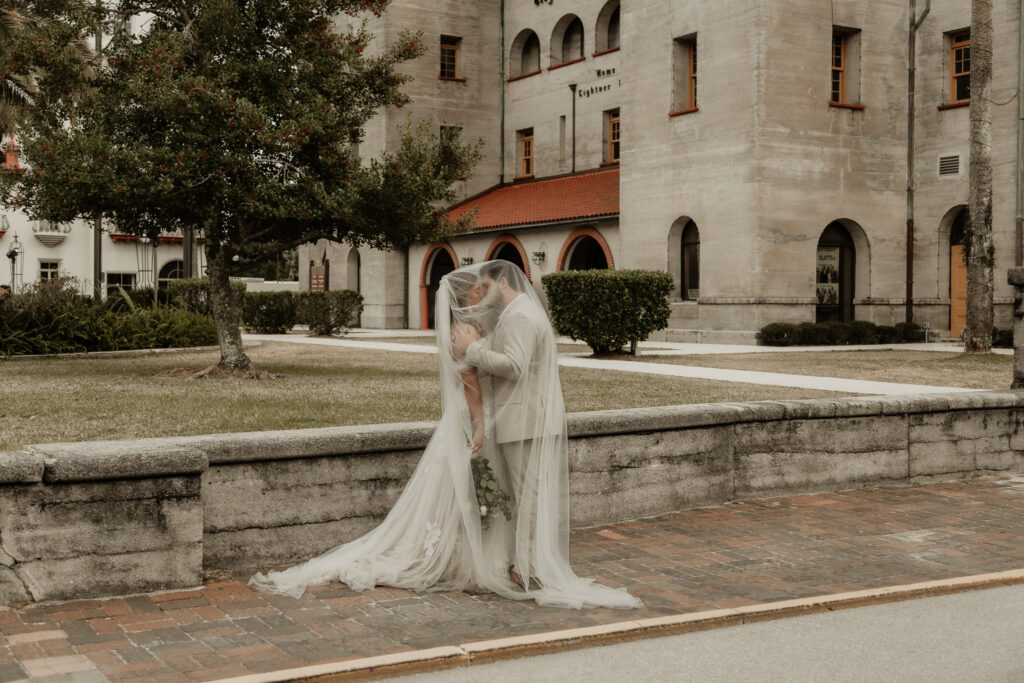 Artistic bride and groom portraits. Bride and groom are under the brides veil kissing on the cobble stone side walk of st augustine