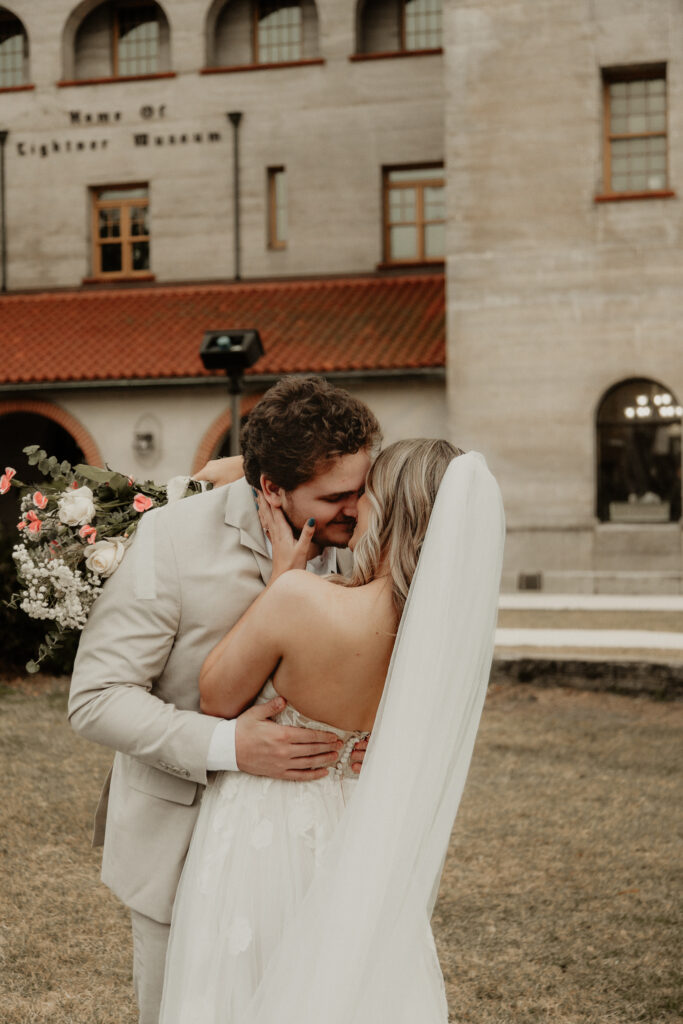 Bride and groom are playfully kissing in front of the Lightner Museum