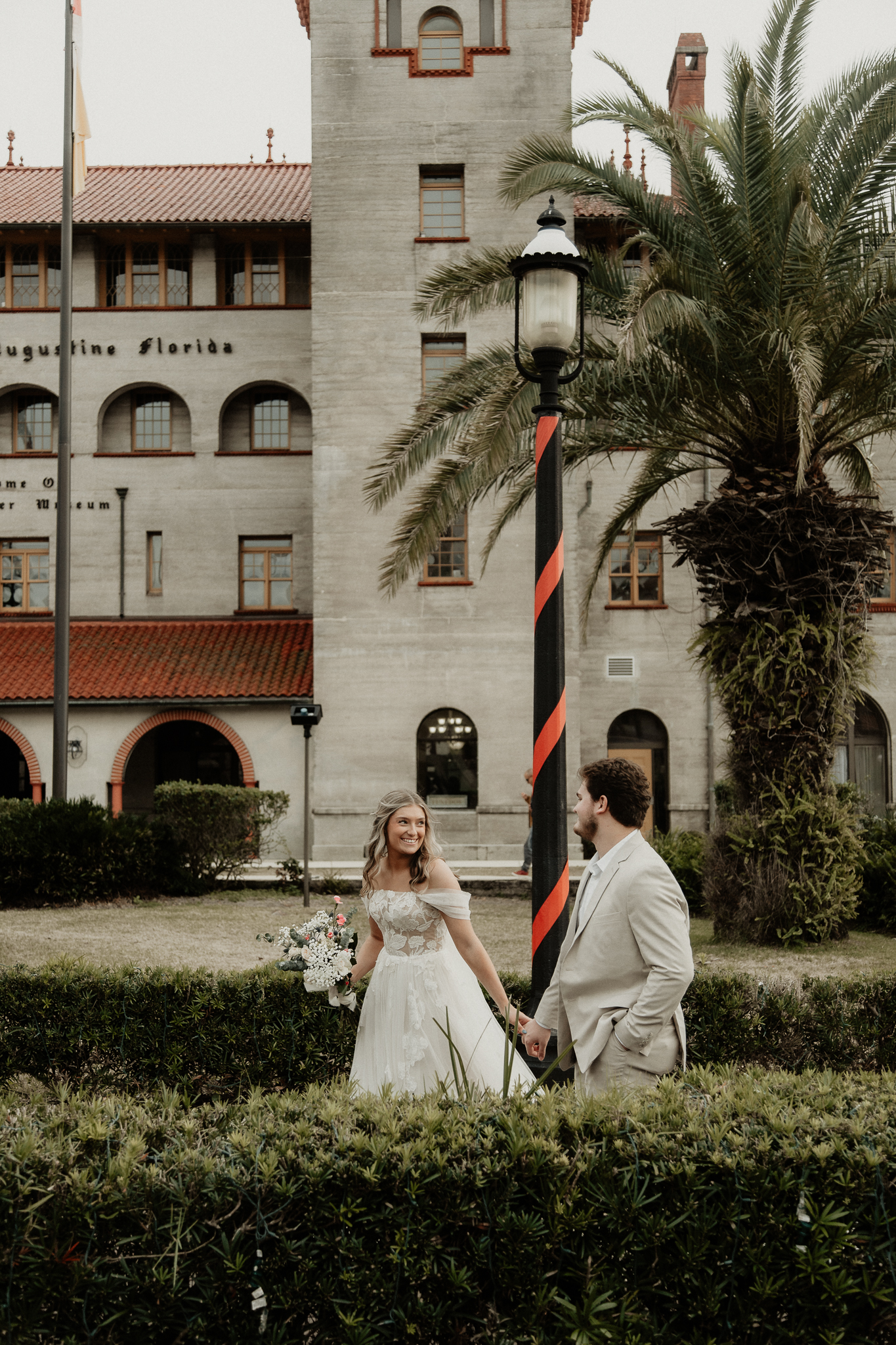 Bride and groom walk hand in hand in front of the lightner museum