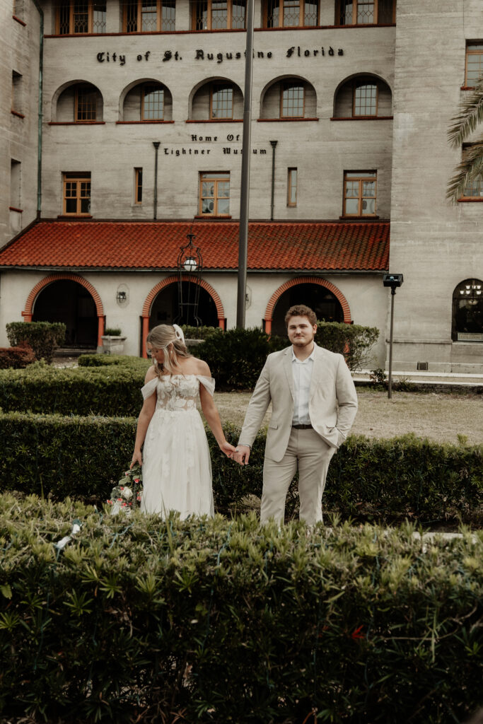 bride and groom are standing hand in hand in front of the lightner museum.