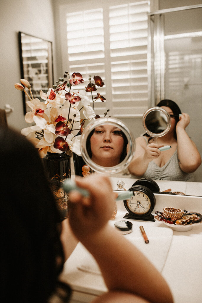 Bride putting on her mascara looking through a hand help mirror